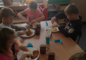 Dzieci używające noża i widelca podczas spożywania kotleta.